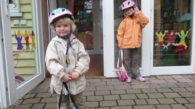 Två glada barn med cykelhjälmar står utanför förskola