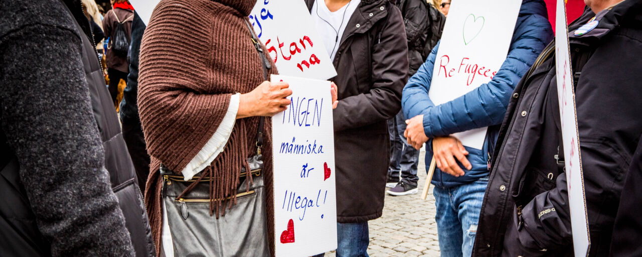 Demonstration för att låta flyktingar stanna. En grupp människor håller i plakat där det står 