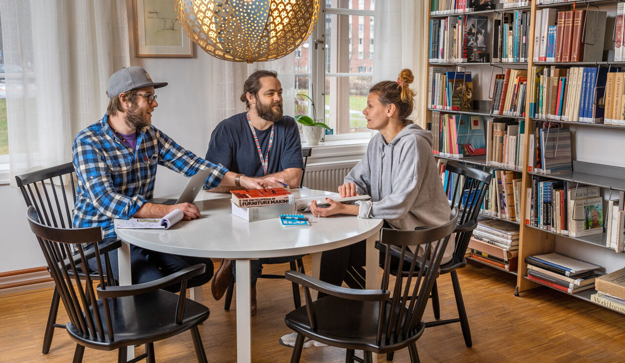 Three students at a round table in front of a book shelf.