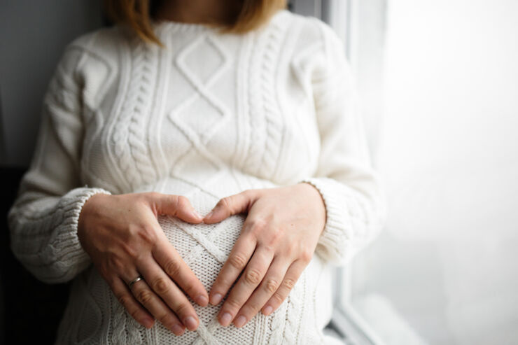 kvinna formar hjärta med händerna över sin gravidmage.
