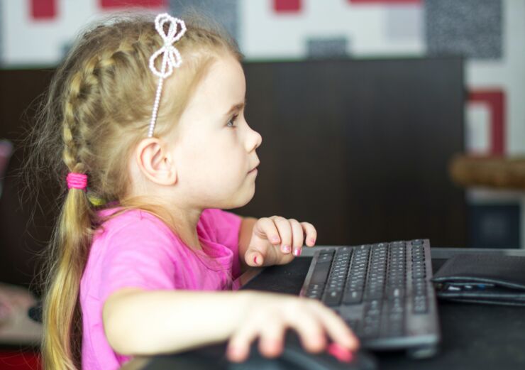 Ung flicka sitter och håller på med en dator.