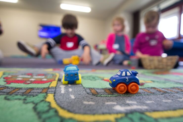 Tre barn sitter och leker med bilar i förgrunden.
