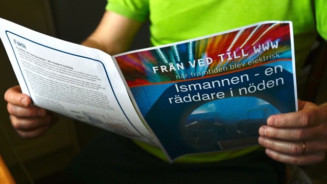 Person sitter och läser tidning med titel "Från ved till WWW".