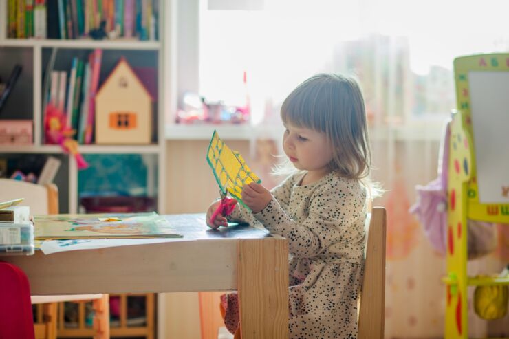 Flicka sitter i barnrum och klipper i ett papper med sax.