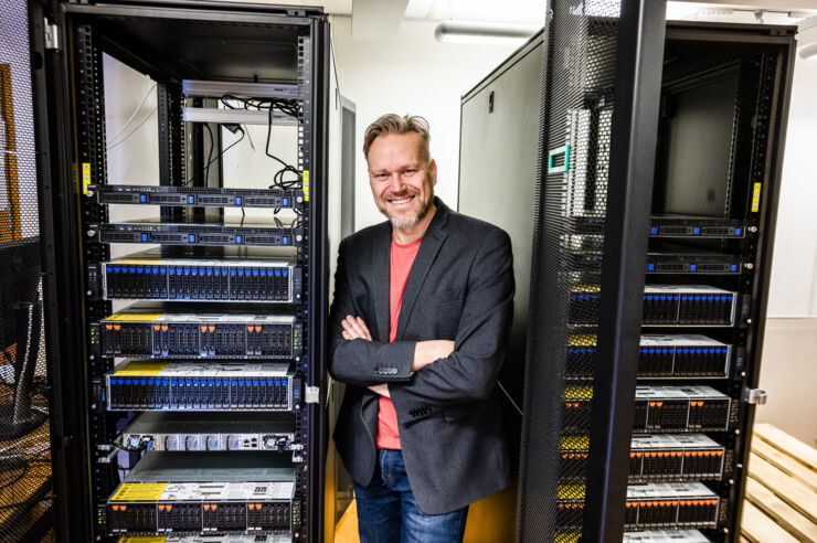 A portrait of Magnus Bång standing in between two shelves filled with electronics