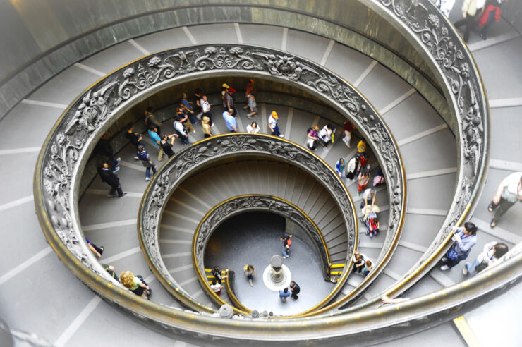 Picture of a spiral staircase taken from above with people walking in the stairway.