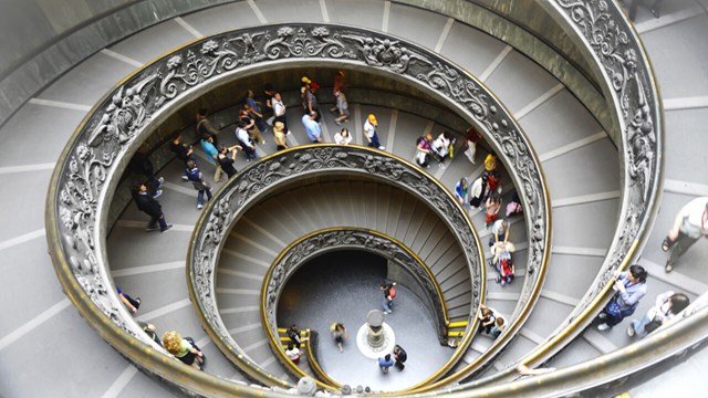 Picture of a spiral staircase taken from above with people walking in the stairway.