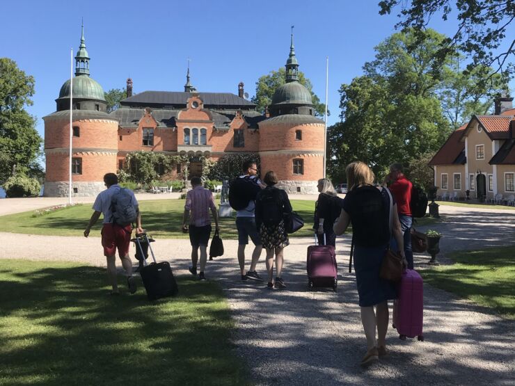 Sju personer går med resväskor mot ett slott.