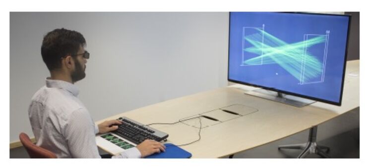 A man sitting at a keyboard with the computer screen placed at a big distance in front of him