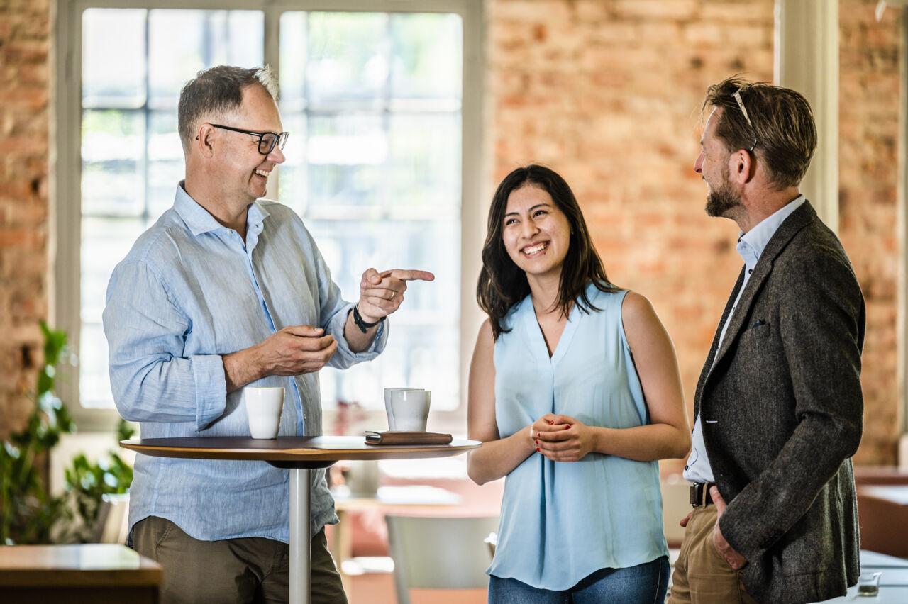 Tre människor står och samtalar, alla är glada.