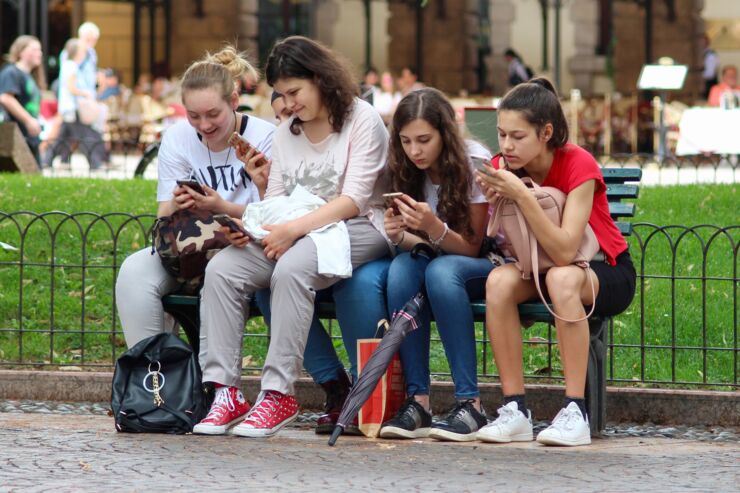 Fyra tonårstjejer på en parkbänk. Alla tittar i sina telefoner