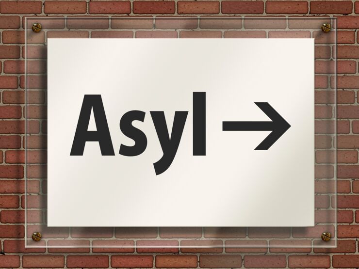 Vit skylt på vägg med text Asyl och en pil