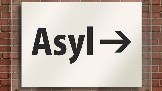 Vit skylt på vägg med text Asyl och en pil