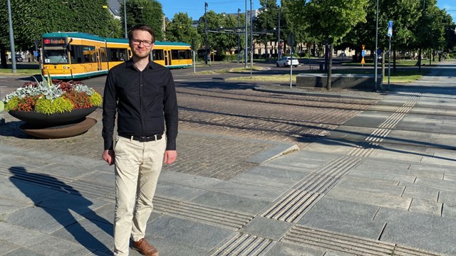 A man standing in front of tram tracks with a tram in the background