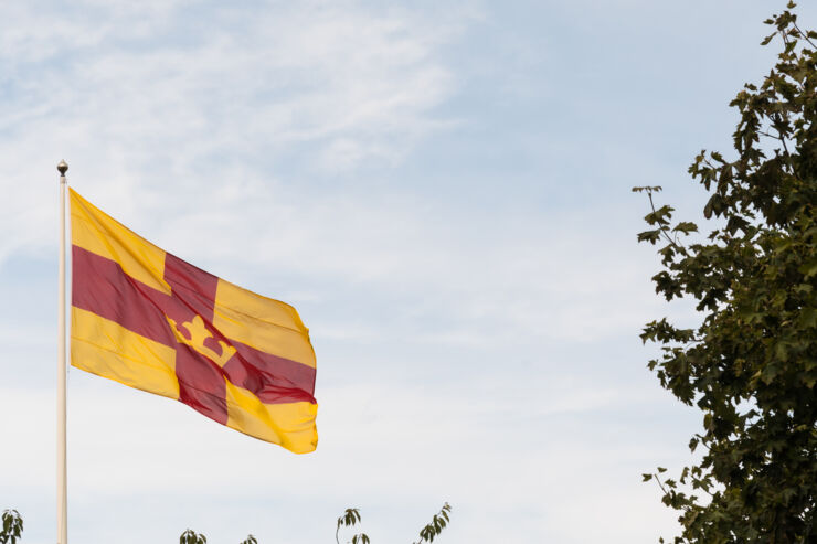 Foto föreställande Svenska kyrkans gula och röda flagga som vajar i vinden framför en blå himmel med några moln