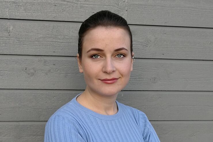 Portrait of a dark-haired young woman in a light blue sweater against a grey wall