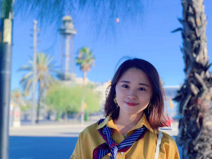 Young asian woman in a yellow shirt in front of palm trees and blue sky