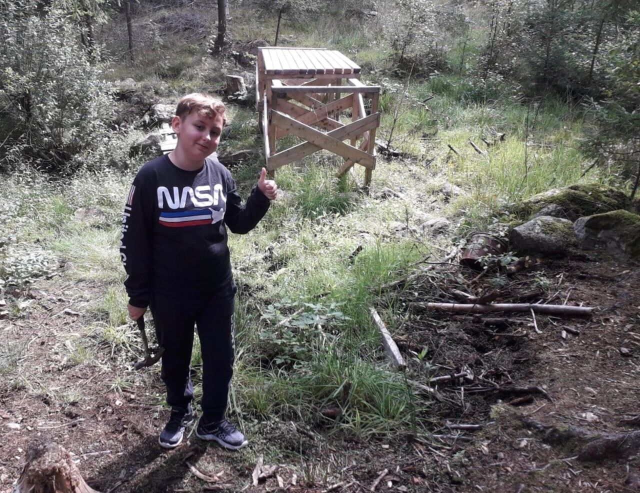 Elev gör tummen upp mot fotograf med hammare i handen i bakgrunden ett bygge.