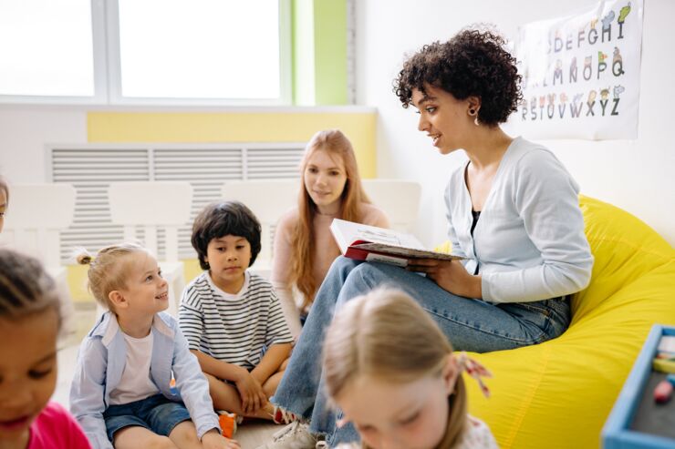 Pedagog sitter med barngrupp och läser bok.