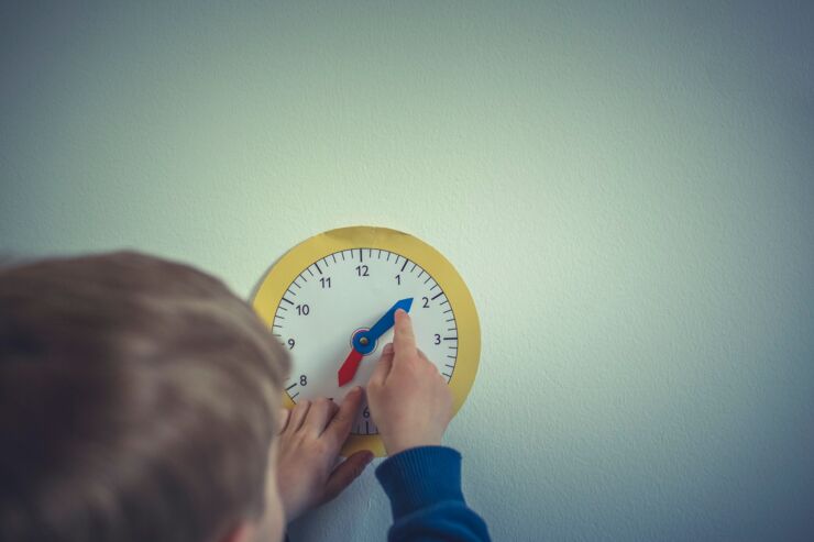 Barn pekar på klocka gjord av papper som sitter på väggen.
