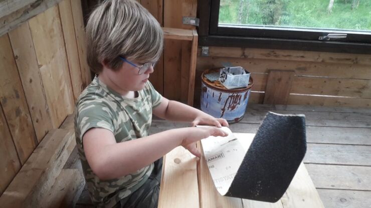 Pojke jobbar i trätorn med sandpapper.