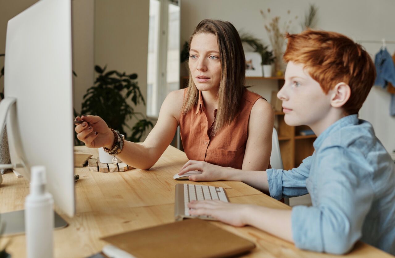 Lärare sitter med elev vid dator och ger instruktioner.