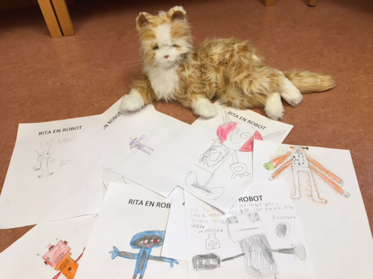 A robot cat lies on the floor along with several drawings of robots that the children did.