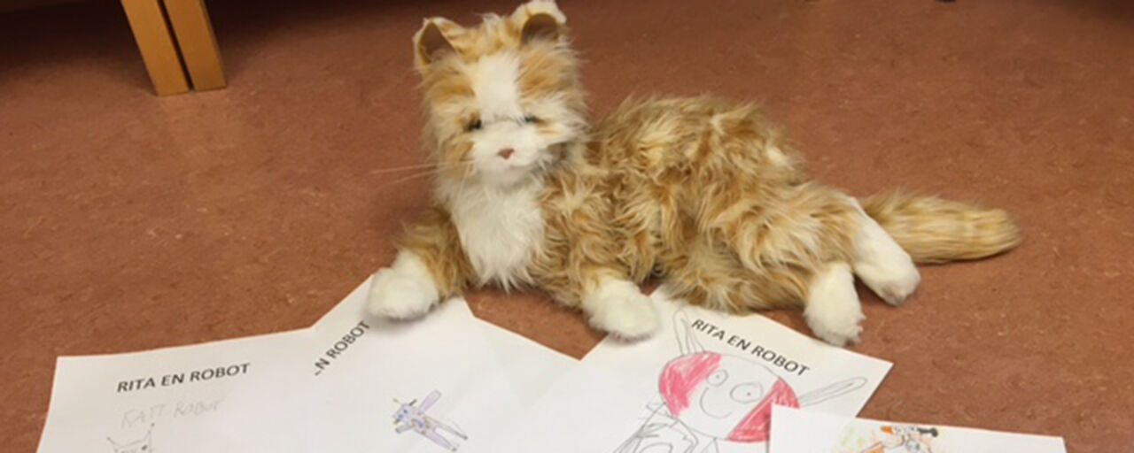 En robotkatt ligger på ett golv med flera teckningar på robotar som barn ritat.