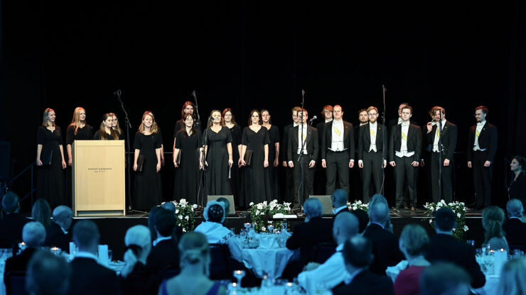 Women in black dresses and men in tailcoats on stage.