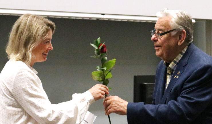 Kvinnlig forskare tar emot blomma från äldre man. 