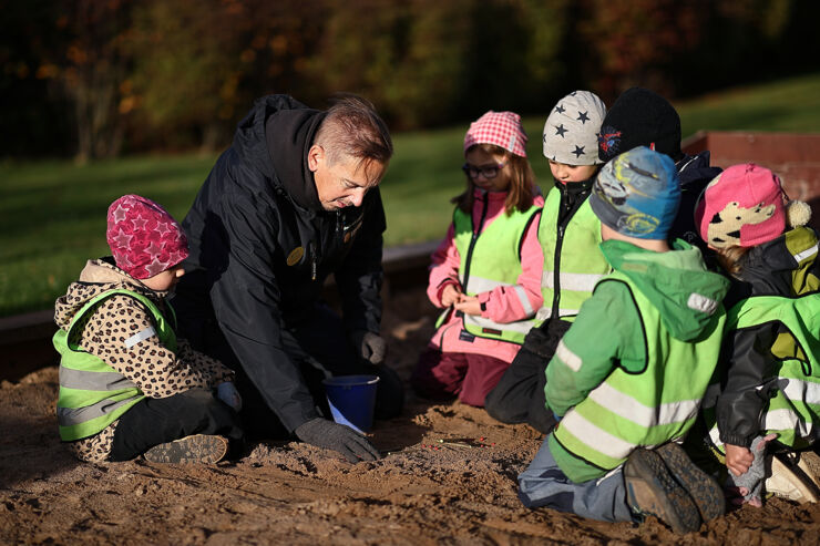 Förskollärare Henrik sitter och leker pedagogiskt med 6 barn i en sandlåda