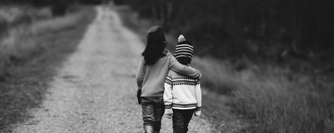 Two children walking along a road with their back turned to the camera.