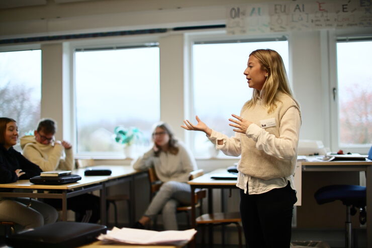 A student teacher stands in a classroom and speaks in front of students.