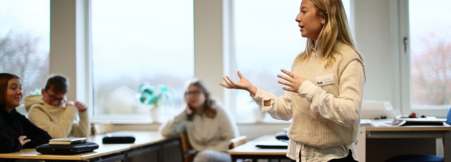 A student teacher stands in a classroom and speaks in front of students.