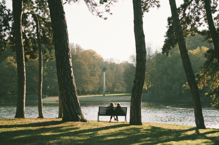 Foto på en park i Malmö. Två personer sitter på en parkbänk och tittar på ett konstverk.