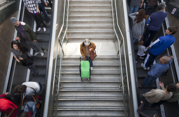 Bild på människor som använder rulltrappor. Mellan rulltrapporna går en äldre person i en vanlig trappa.