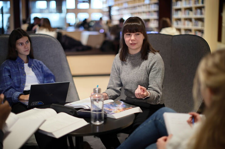 Tre studenter sitter och pluggar och diskuterar på biblioteket på Campus Valla.