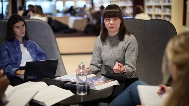 Tre studenter sitter och pluggar och diskuterar på biblioteket på Campus Valla.