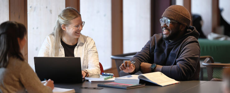 Tre studenter sitter och pluggar och diskuterar inne i biblioteket på Campus Valla. 