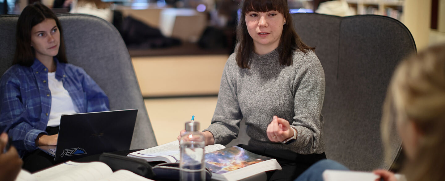 Tre studenter sitter och pluggar och diskuterar inne i biblioteket på Campus Valla. 