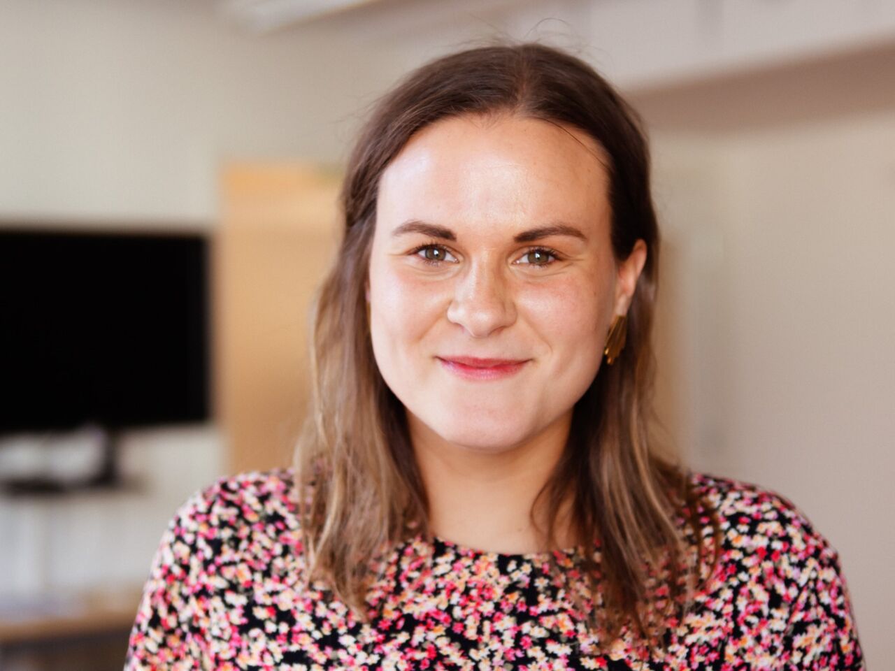 Närbild av glad ung kvinna med brunt hår och blommig blus