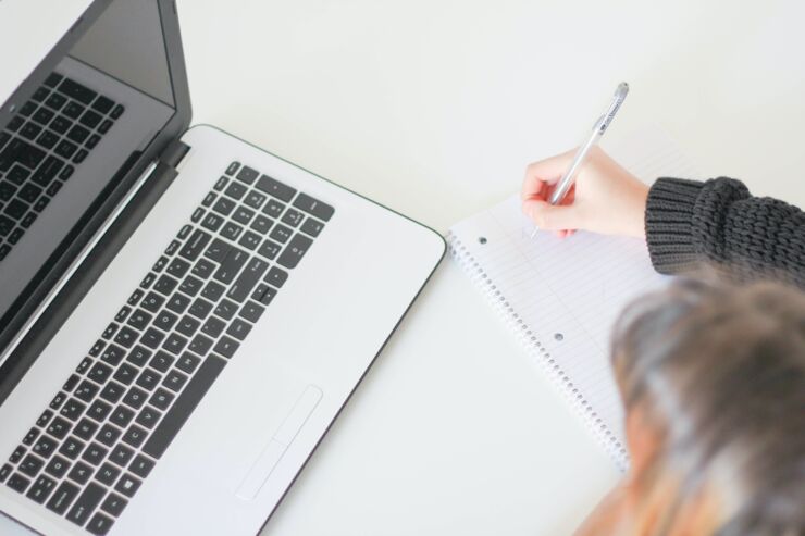 A photo of a computer, in the corner an arm taking notes is visible.