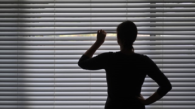 Woman in dark room, trying to look outside