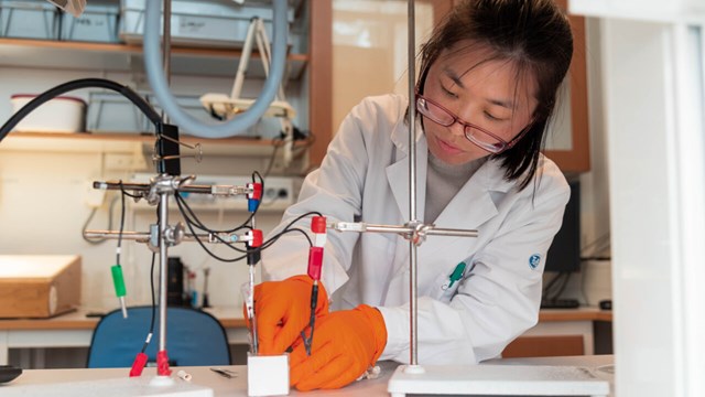 En kvinnlig doktorand monterar experimentuppställningen.