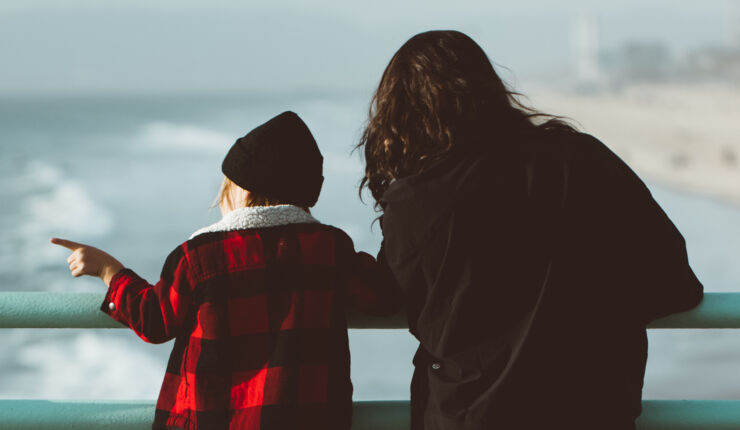 Ett barn och en vuxen ser ut över havet.