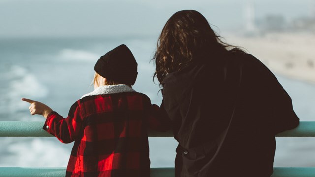 A child and an adult standing next to each other looking at the sea.