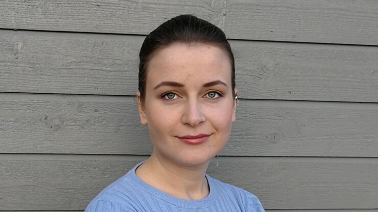 Portrait of a dark-haired young woman in a light blue sweater against a grey wall