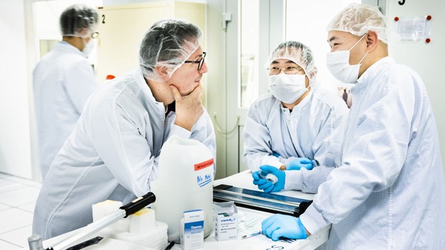Three people in LOE dressed in lab-coats, disposable caps and protective masks. 