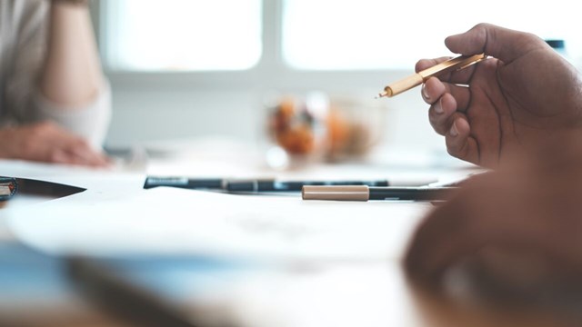 Papper på ett bord och en hand som håller i en penna.