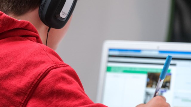 En elev med hörlurar sitter framför en dator och skriver.
